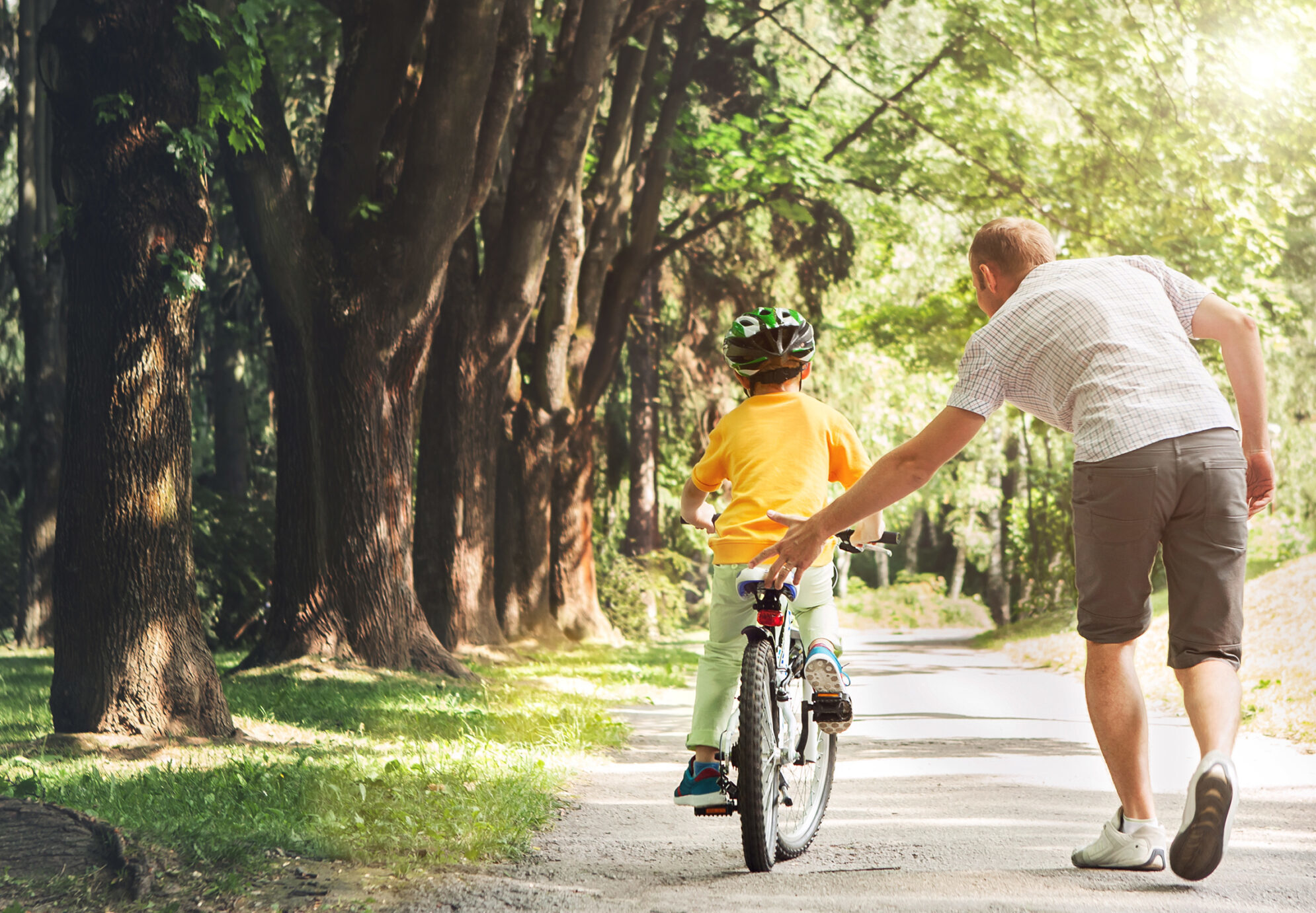 Adult helping boy learn to ride a bicycle